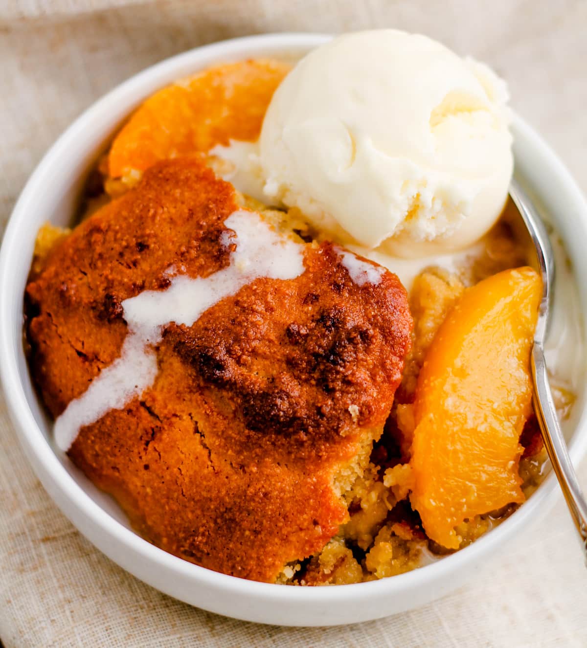 a bowl of healthy peach cobbler with ice cream melting on top.
