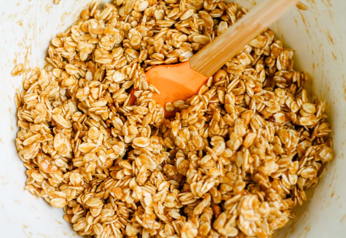 Oats being stirred with a peanut butter mixture in a bowl.