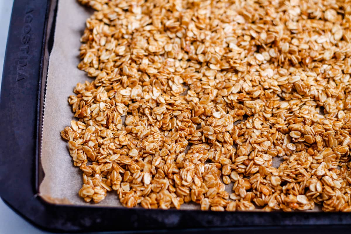 Granola mixture spread evenly onto a baking sheet lined with parchment paper.