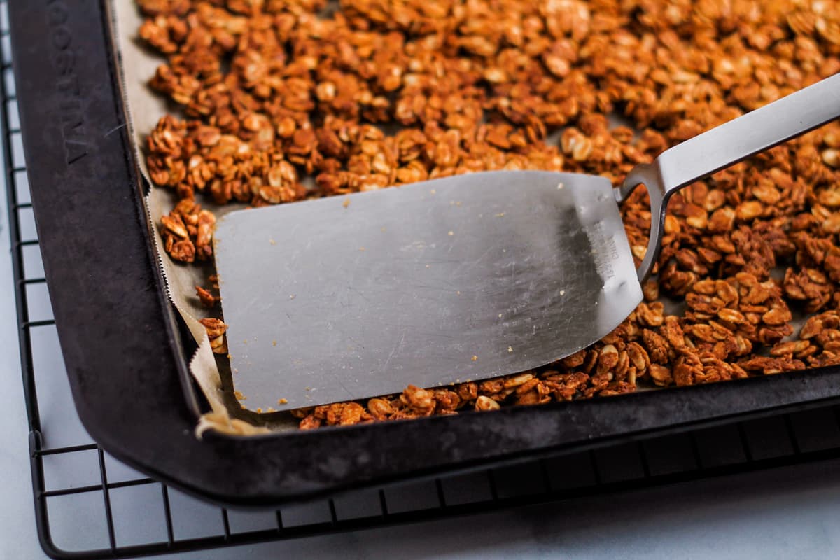 A flat spatula pressing down on a granola mixture in a pan.