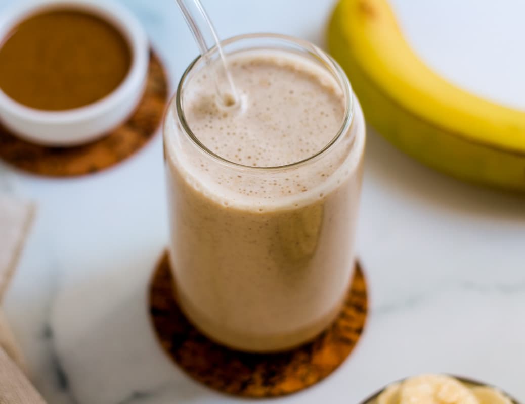A banana almond butter smoothie in a glass with a straw.