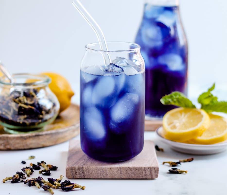 A glass of blue butterfly pea flower tea on a coaster.