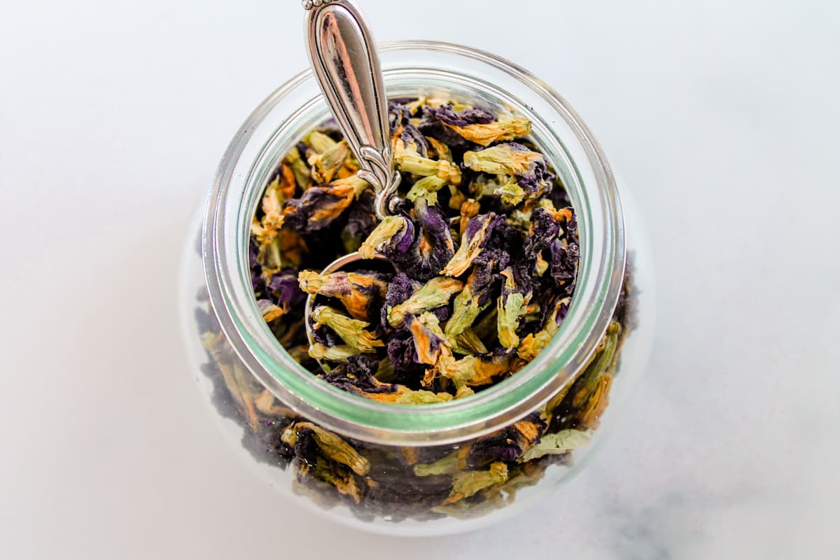 A jar of butterfly pea flower tea with a teaspoon in it.