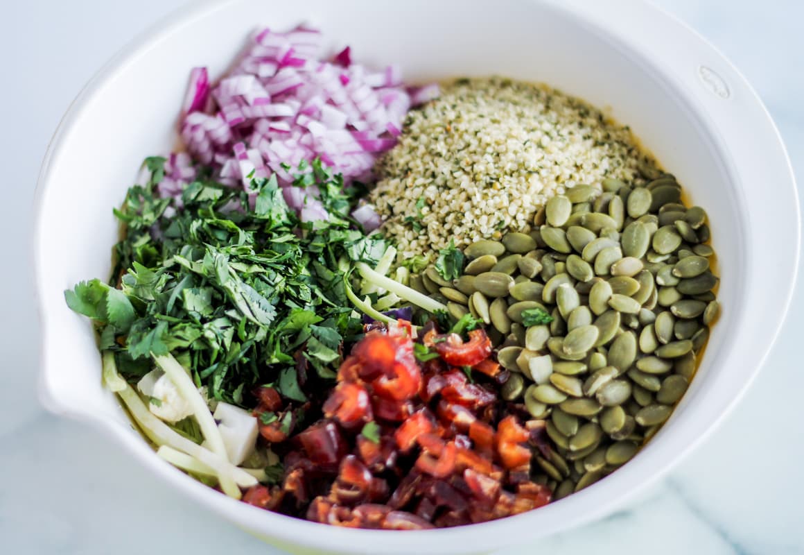 A bowl with mixed veggies, nuts, seeds and dates