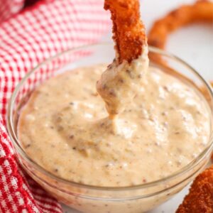 An onion ring being dunked into dipping sauce in a small bowl.