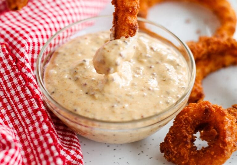 A baked onion ring being dunked into dipping sauce in a small bowl.