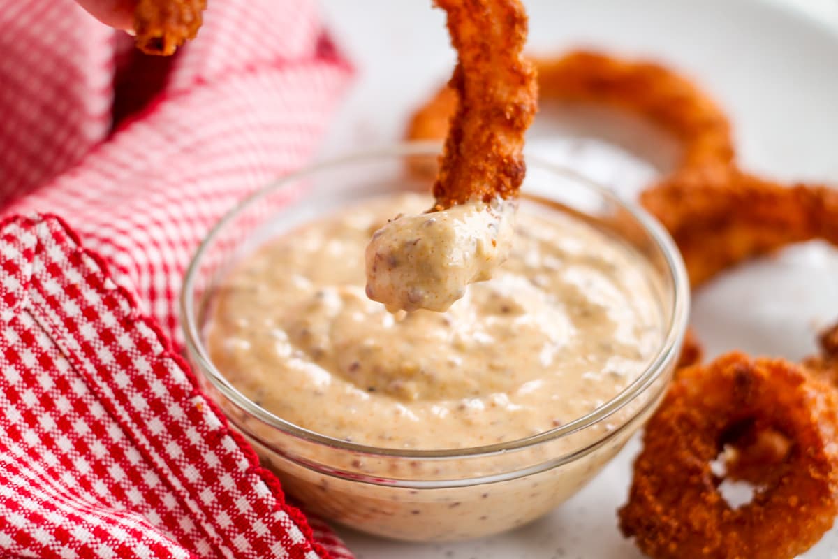 Dipping sauce in a bowl being served with onion rings.