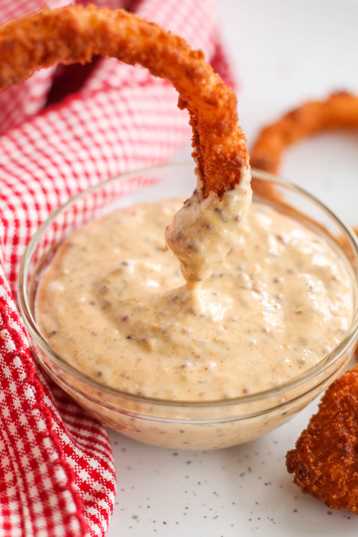 An onion ring being dunked into a small bowl of dipping sauce.