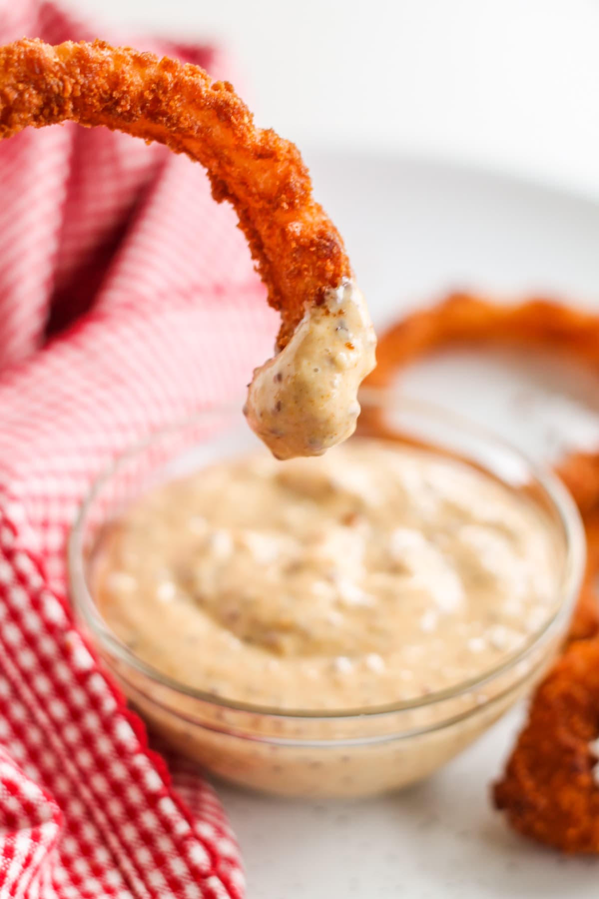 Dipping sauce in a small glass bowl with a baked onion ring being dipped into it.