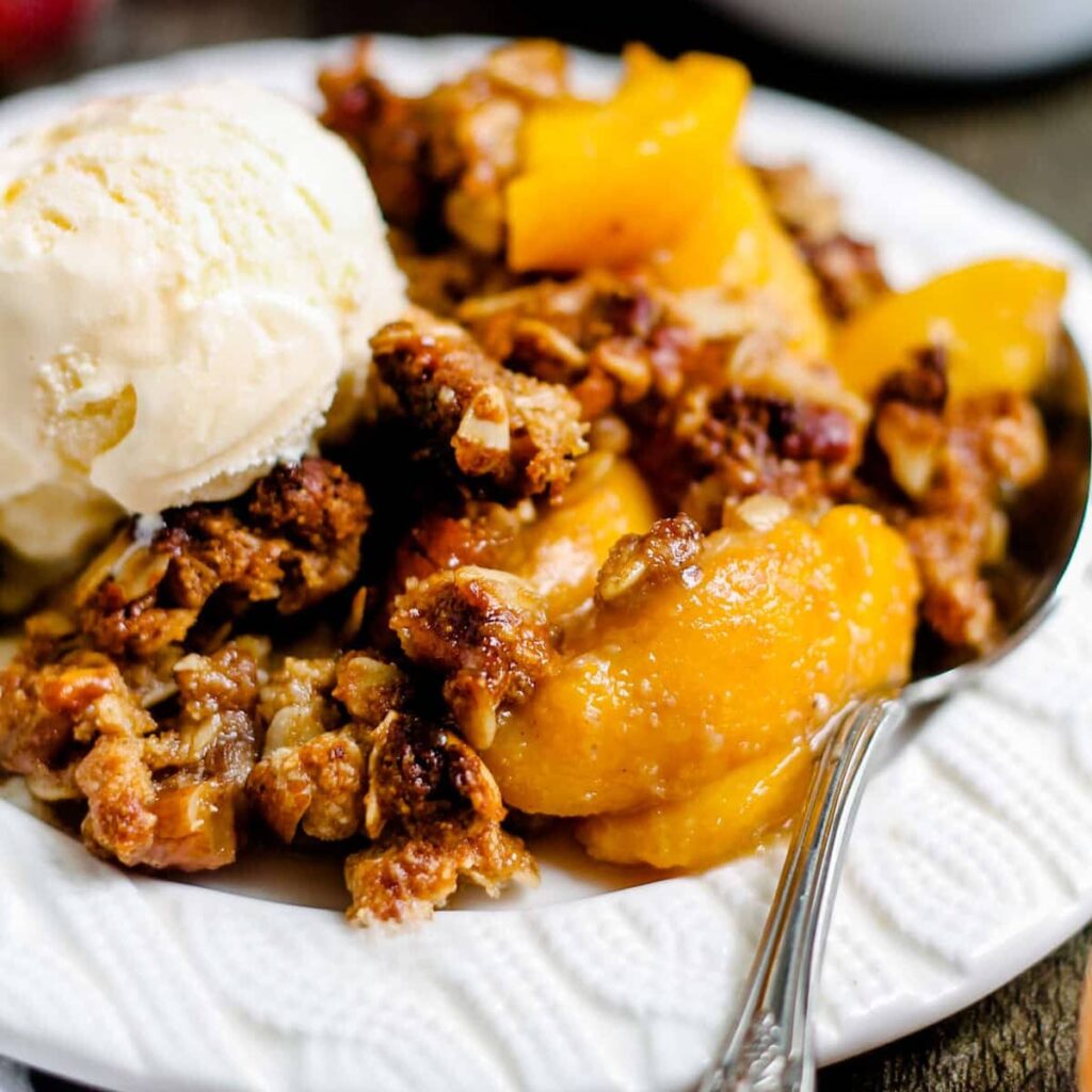A plate of healthy peach crisp topped with vanilla ice cream.