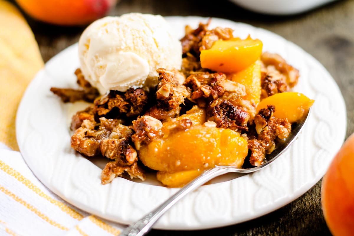 A plate of peach crisp topped with vanilla ice cream.