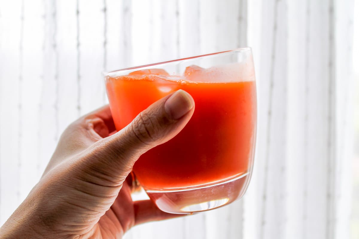 A hand holding a glass with a brightly colored drink.