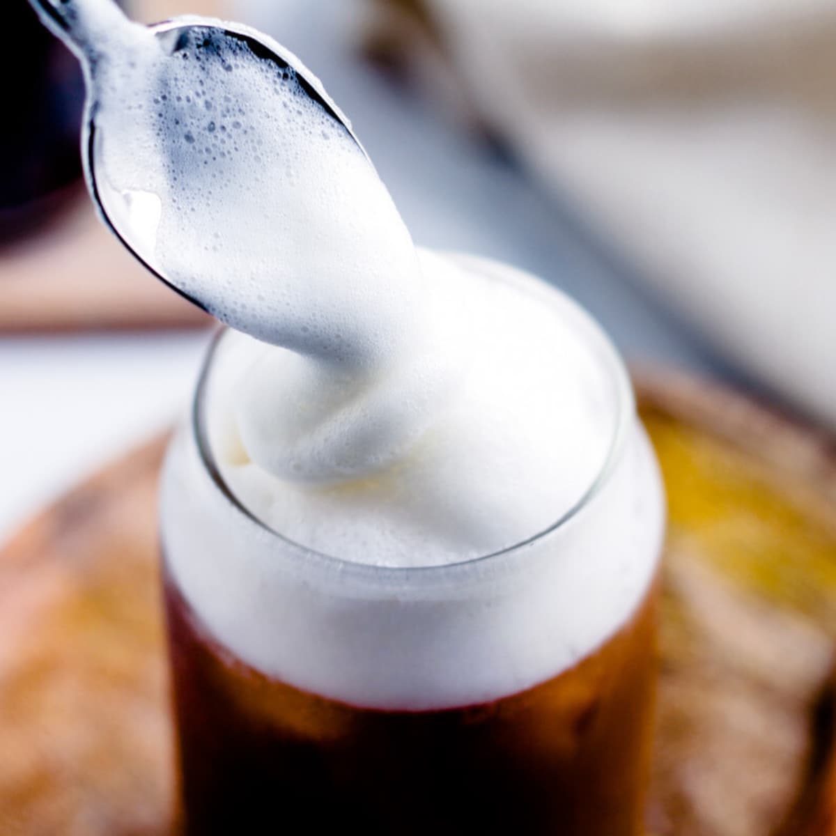 Vanilla cold foam being spooned on top of iced coffee.