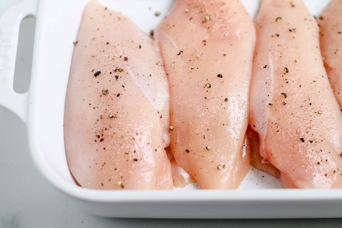 Raw breasts in a baking dish sprinkled with salt and pepper.