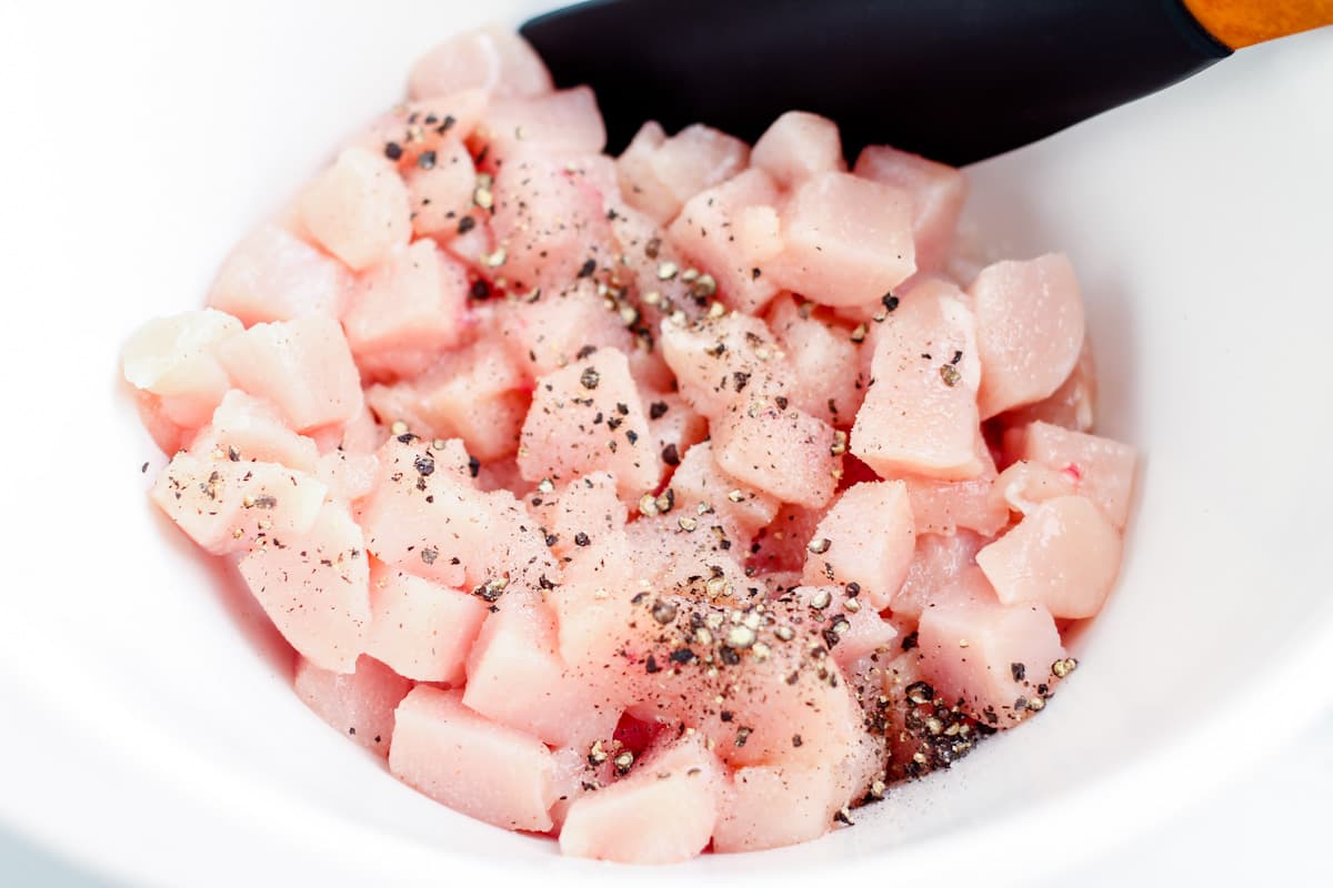 Pieces of raw chicken sprinked with salt and pepper in a mixing bowl.