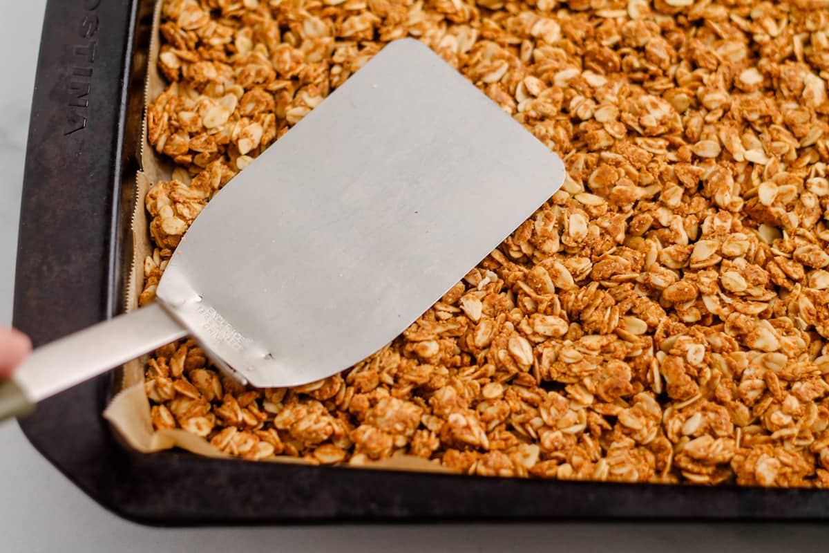 A spatula pressing down onto a baked oat mixture.