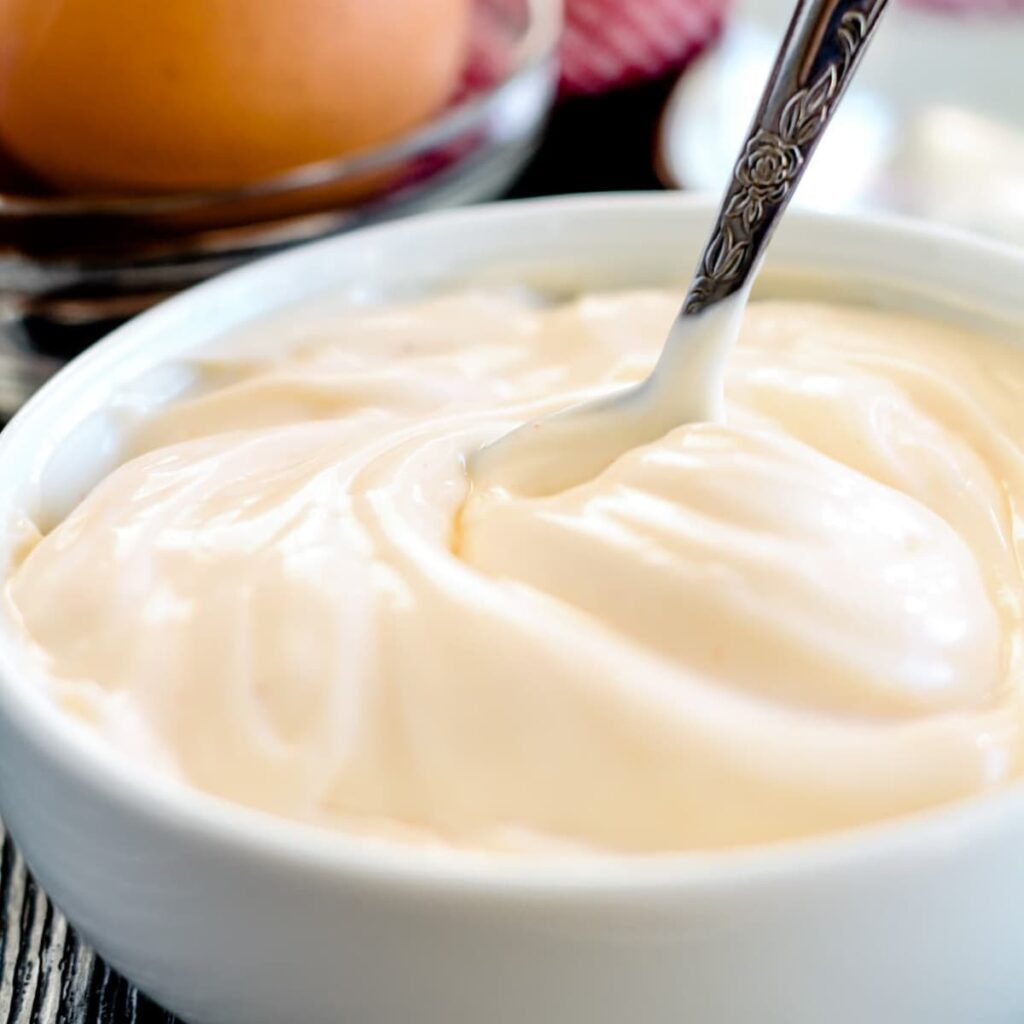 A spoon stirring homemade mayonnaise in a bowl.