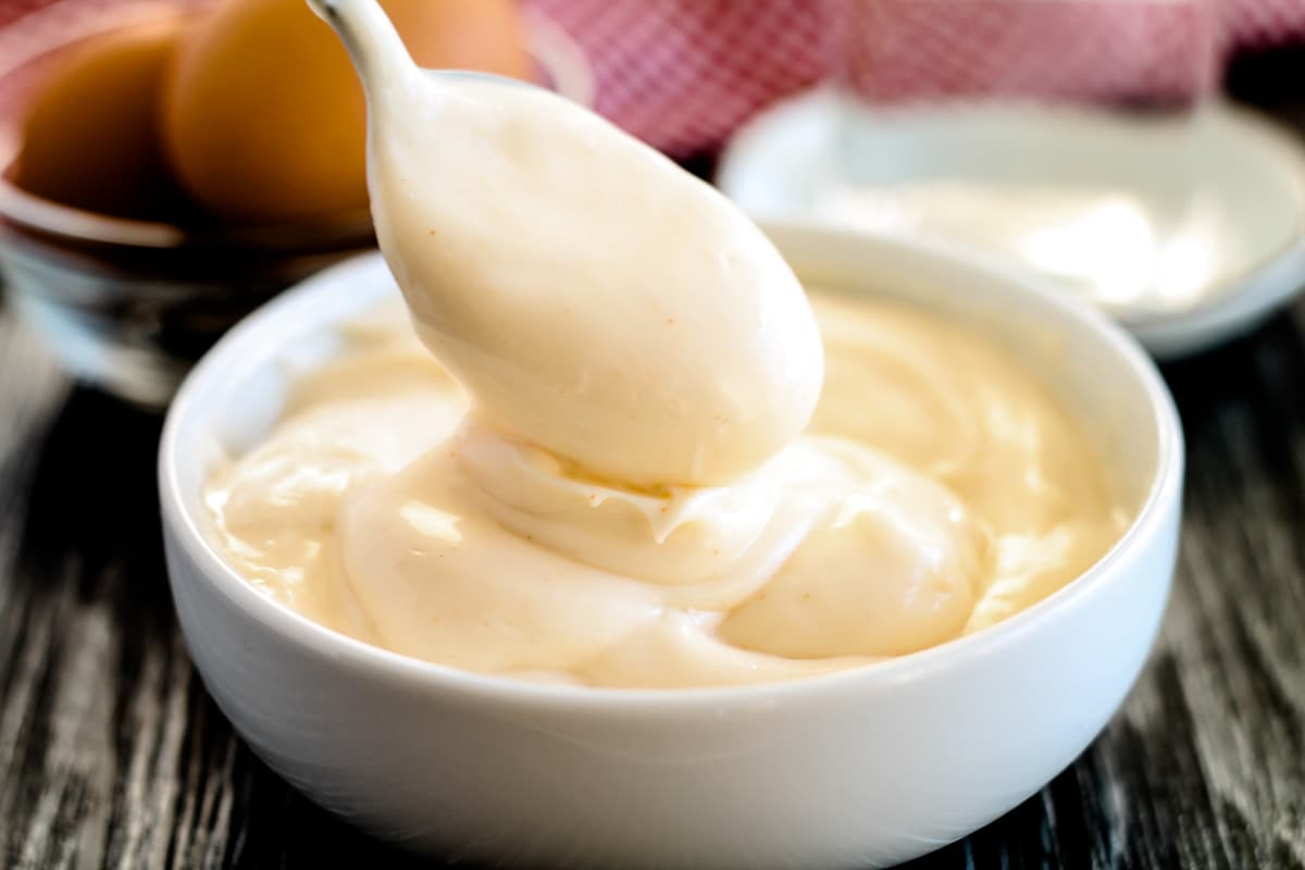 A spoon scooping out lemon mayonnaise from a small bowl.