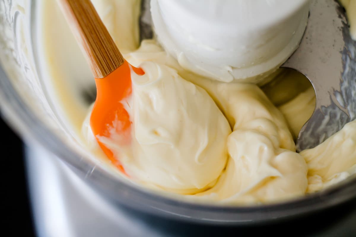 A spatula scooping up homemade lemon mayonnaise from a blender.