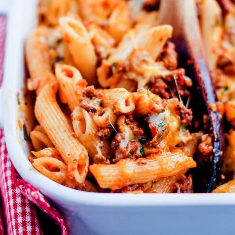 A wooden spoon scooping penne pasta bake from a casserole dish.