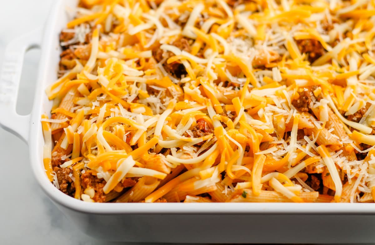 Sauce and noodles mixture in a baking dish covered in shredded cheese.