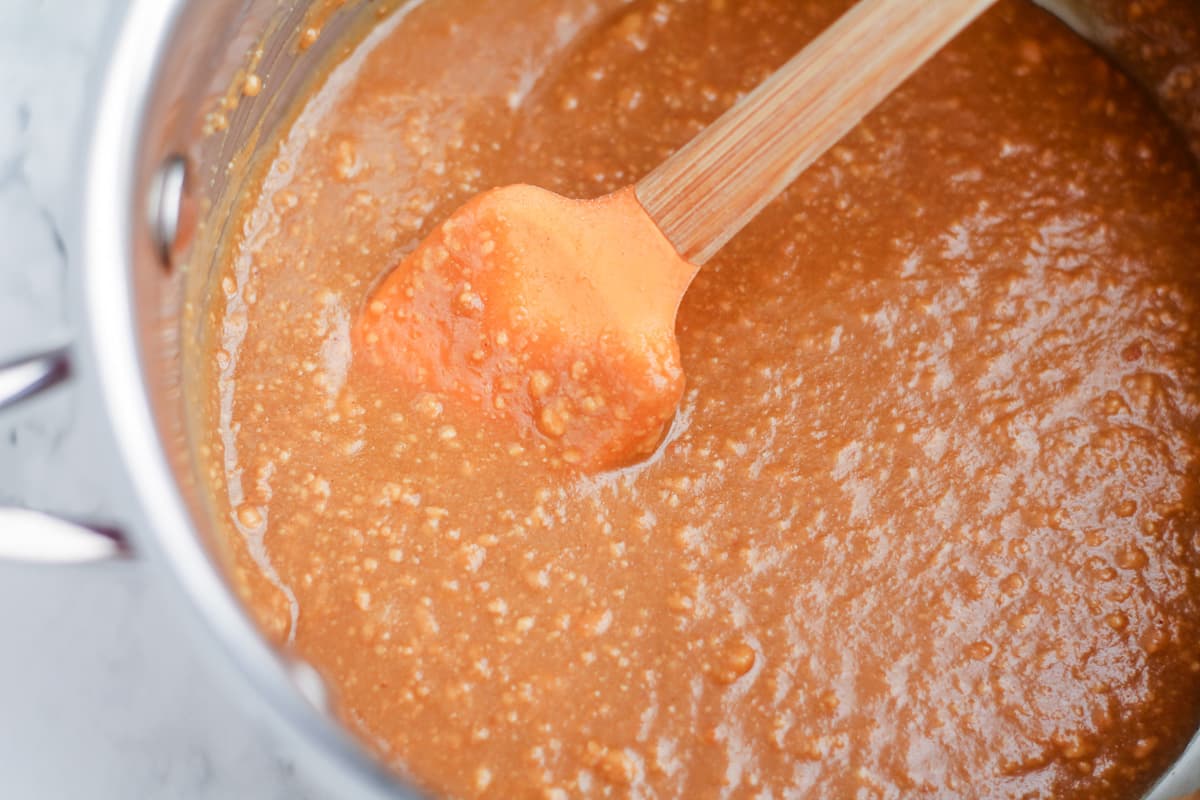 Peanut butter and maple syrup being stirred together in a saucepan.