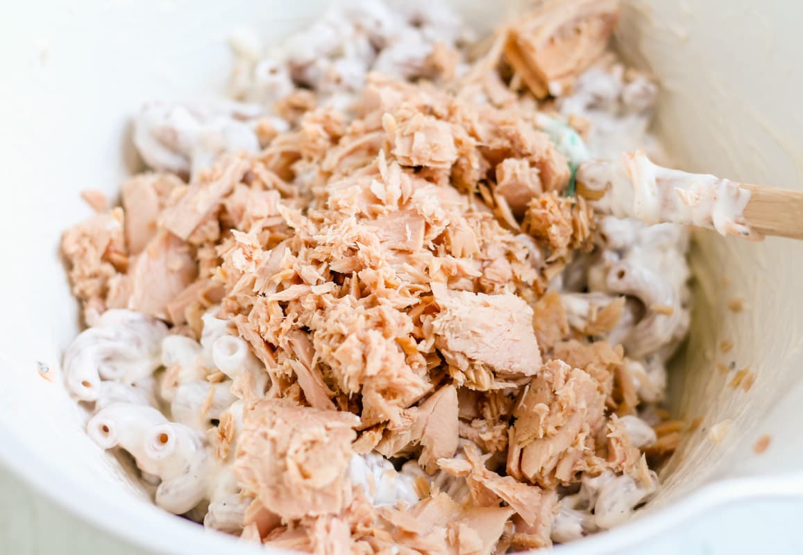 Tuna being added to a bowl of pasta with a creamy sauce.