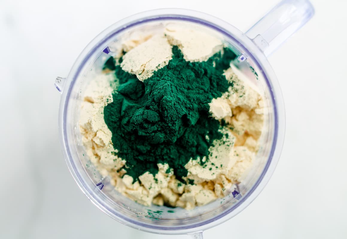 Protein powder and a green powder in a blender.