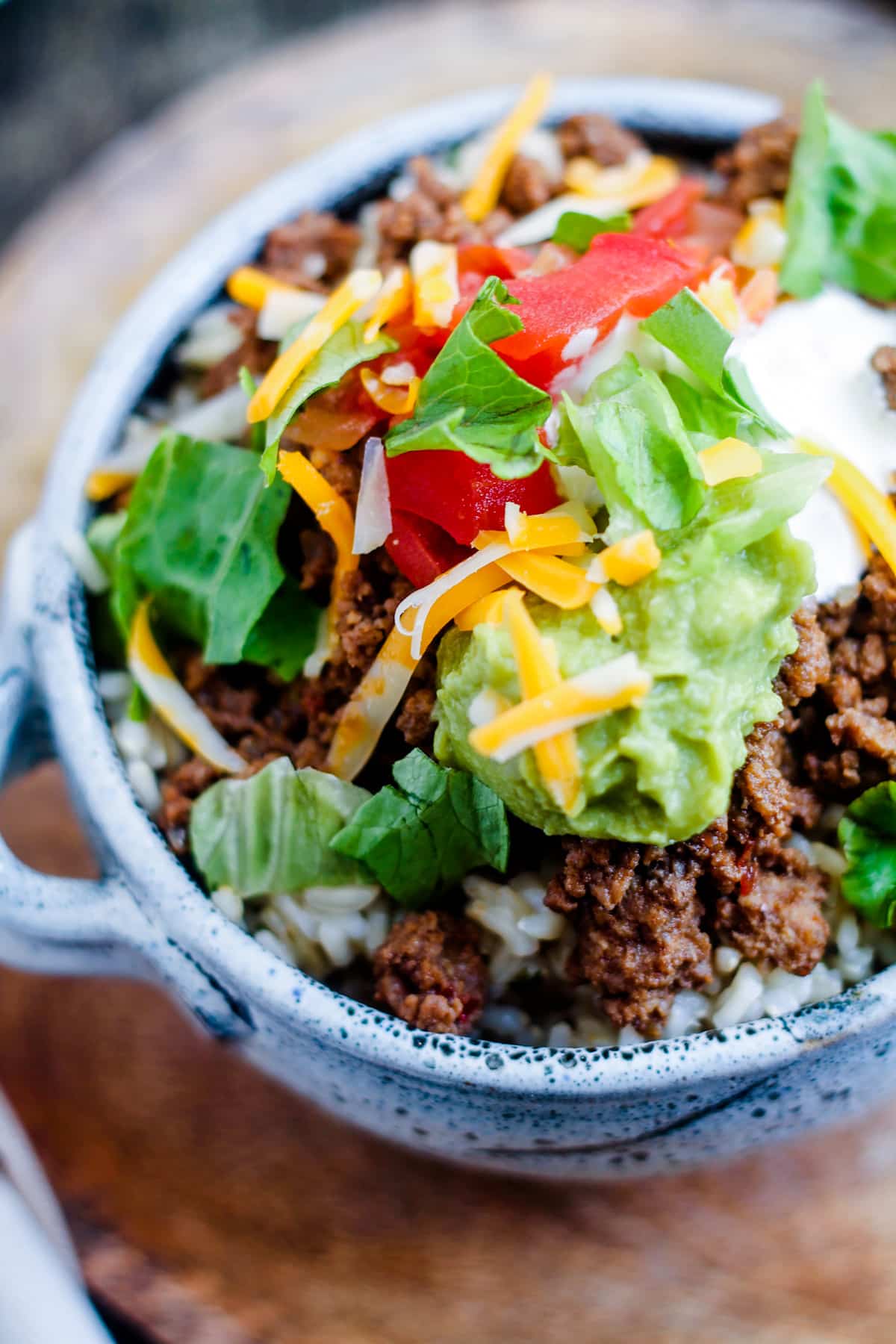A taco rice bowl topped with salsa, cheese, sour cream and guacamole.