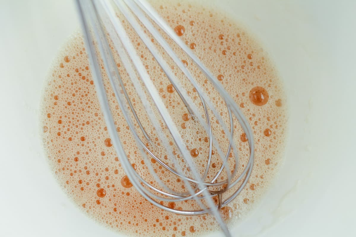 A whisk in a bowl with a frothy liquid.