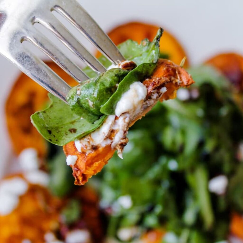 A forkful of arugula salad with goat cheese and sweet potato.
