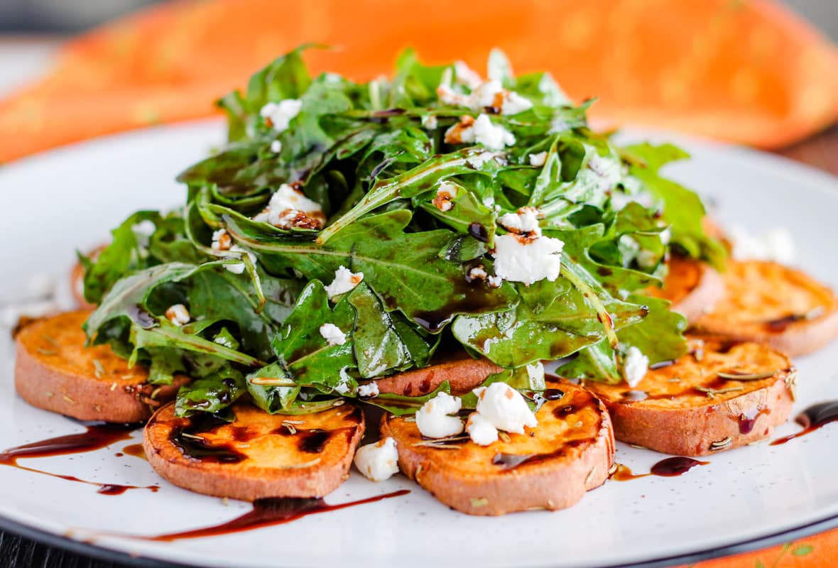 A plate of arugula salad with goat cheese and roasted sweet potatoes.