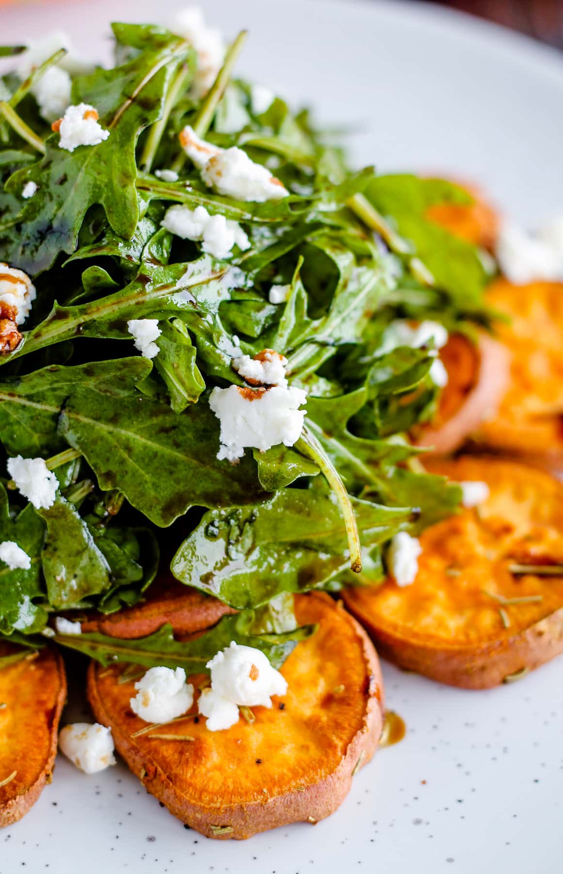Arugula salad topped with crumbled goat cheese served on top of roasted sweet potatoes and drizzled with balsamic glaze