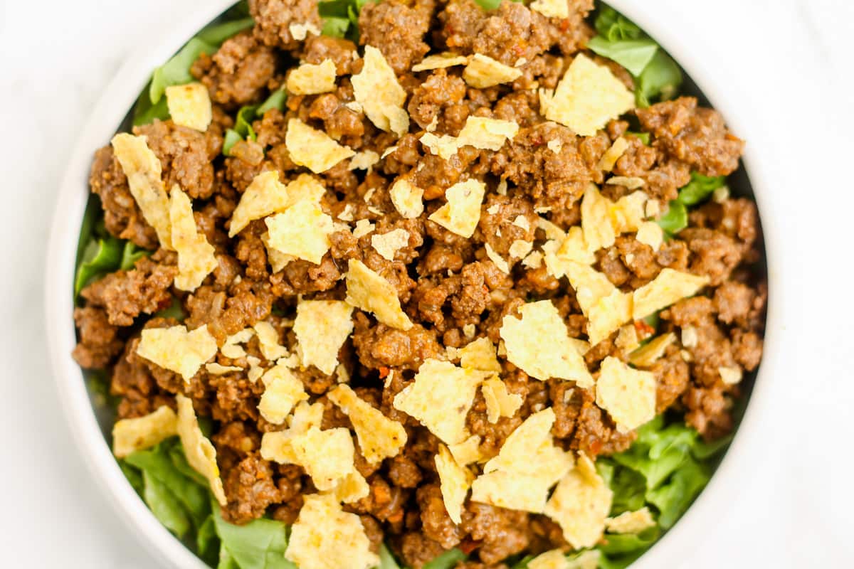 Tortilla chips crumbled on top of a bed of lettuce and spiced beef.