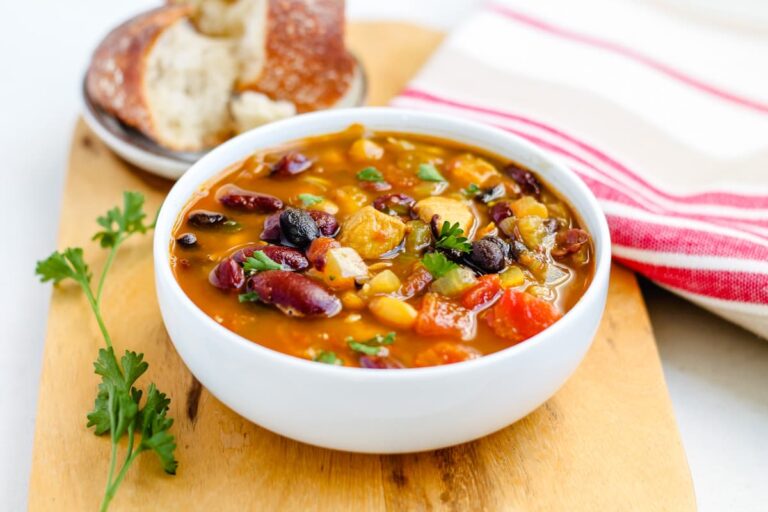 A bowl of three bean chicken soup on a wooden serving board.