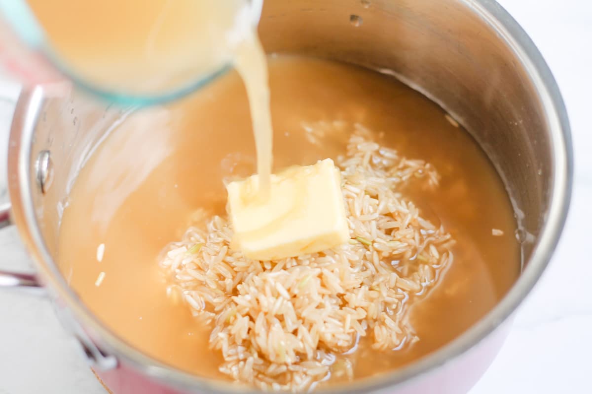 Liquid being poured over grains and butter in a pan.