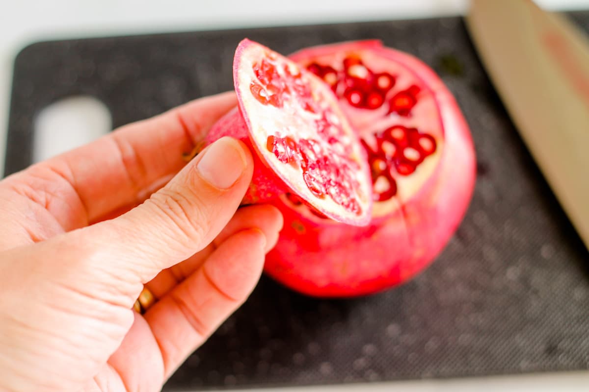 A hand holding the top of a pomegranate that has been sliced off.