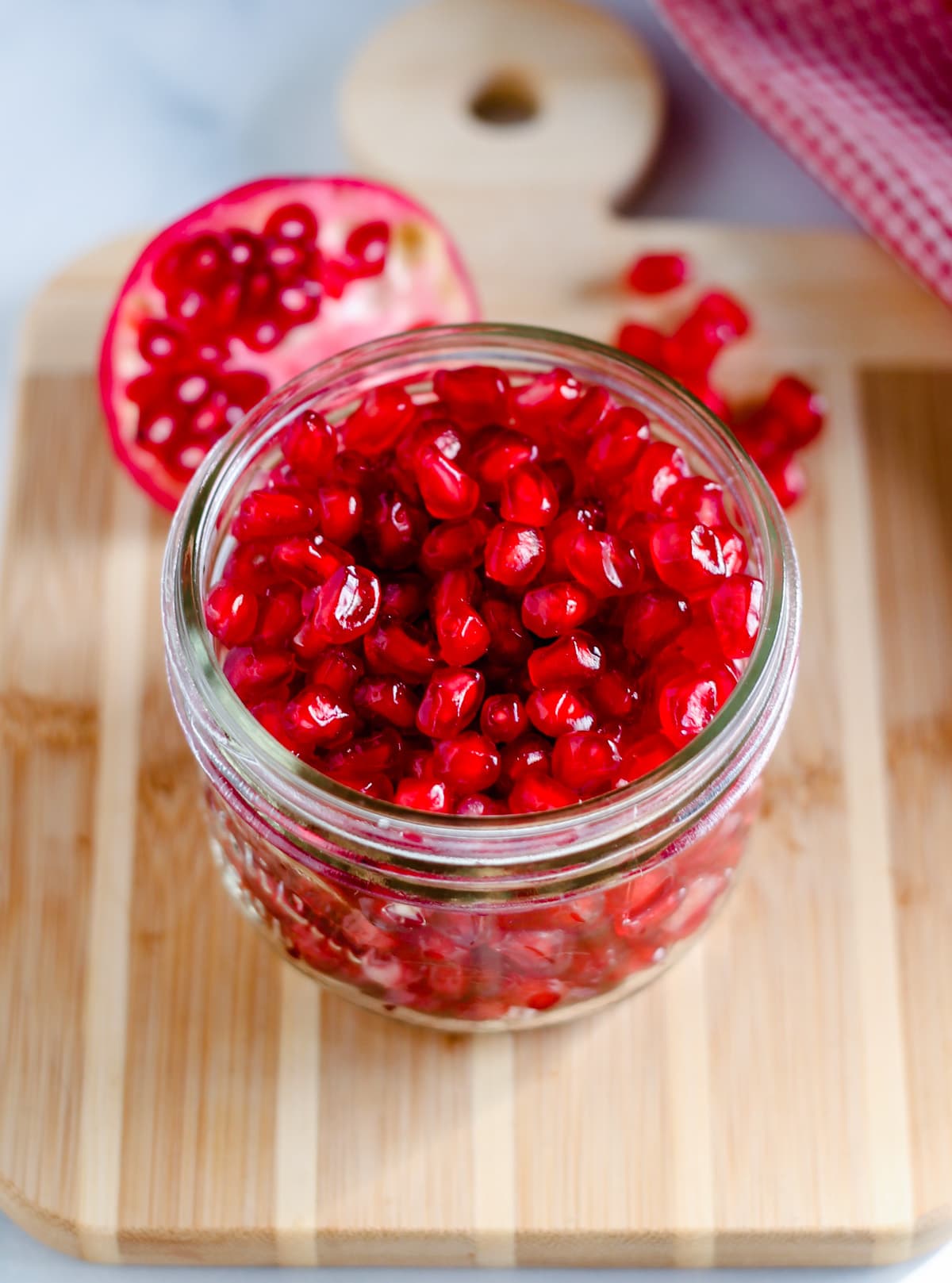 A jar of pomegranate seeds on a wooden board.