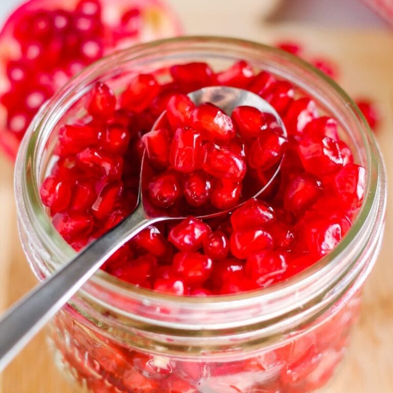 A jar of pomegranate seeds with a spoon in it.