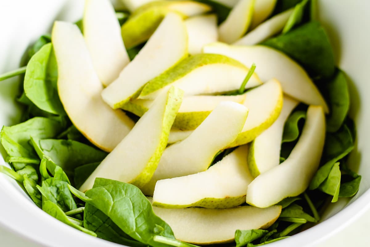 Pears added on top of green leaves in a bowl.