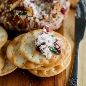 A cranberry pecan cheese ball on a serving board with crackers.
