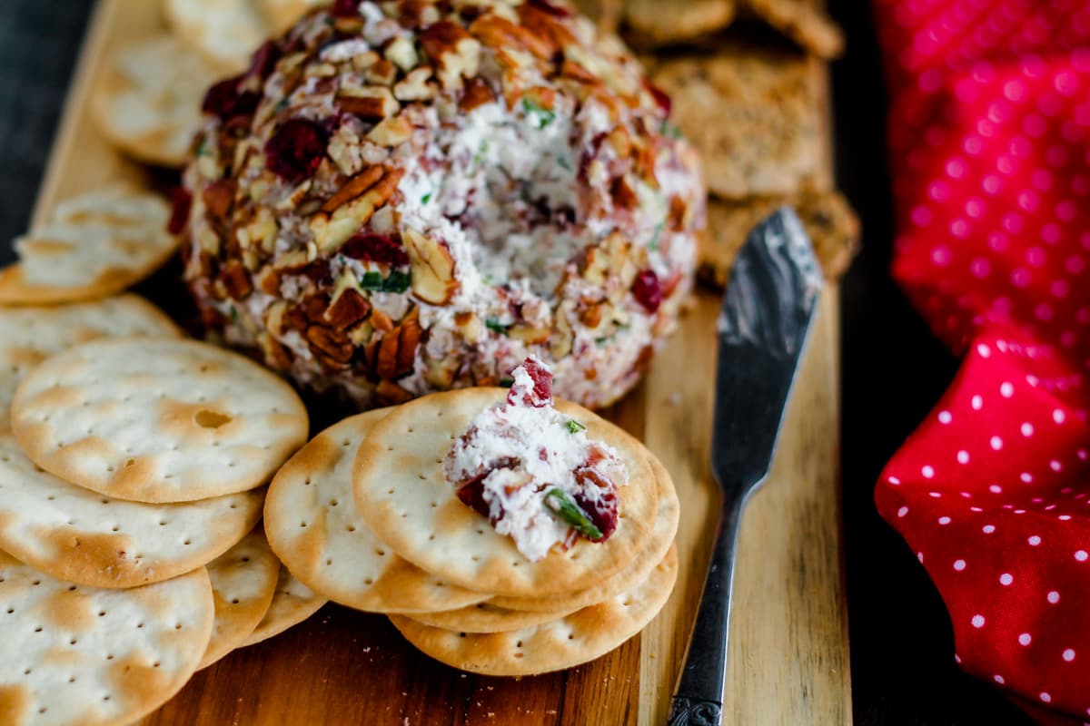 Crackers and a cranberry pecan cheese ball on a wooden board.