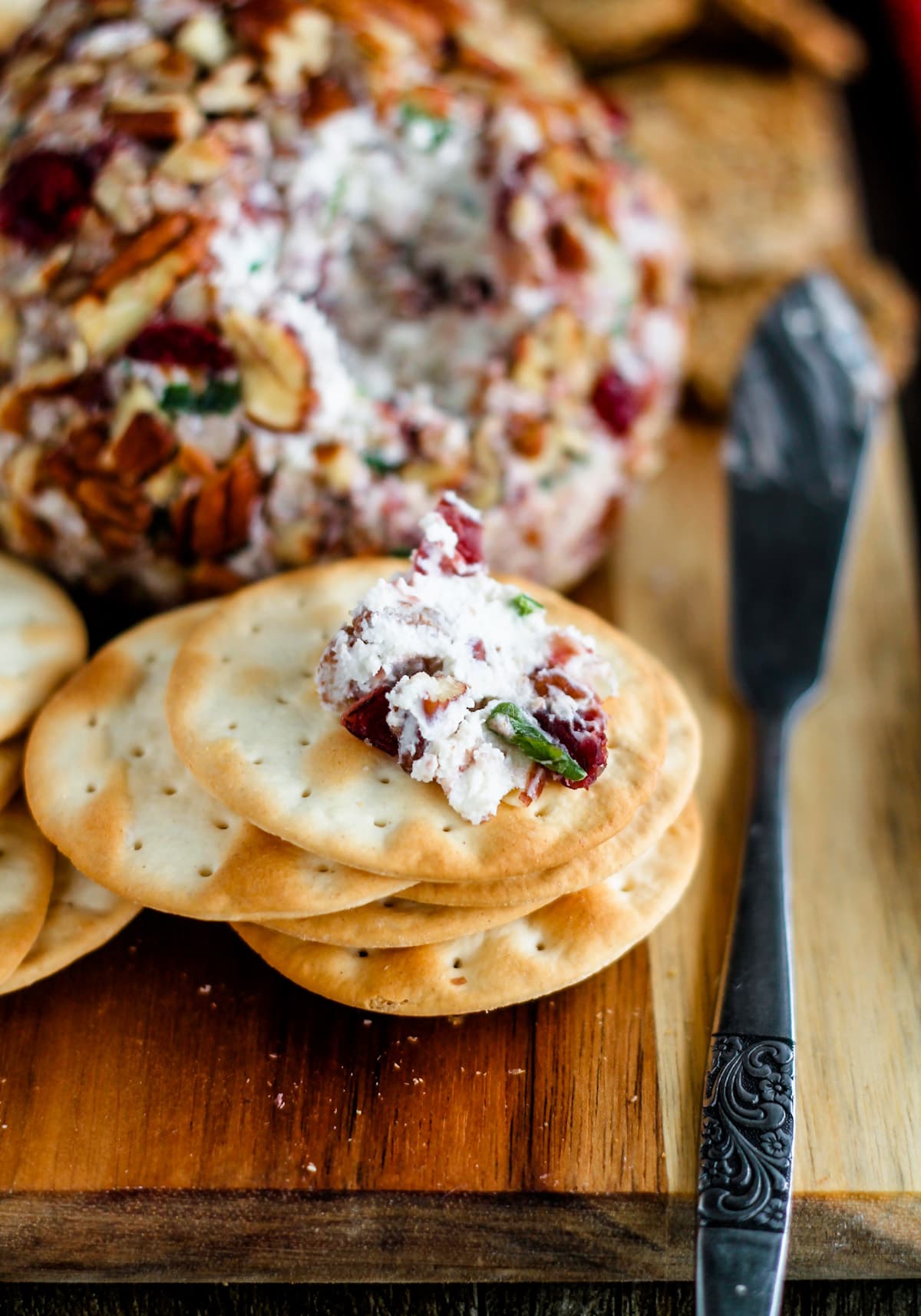 A board with a cranberry pecan cheese ball and a stack of crackers.