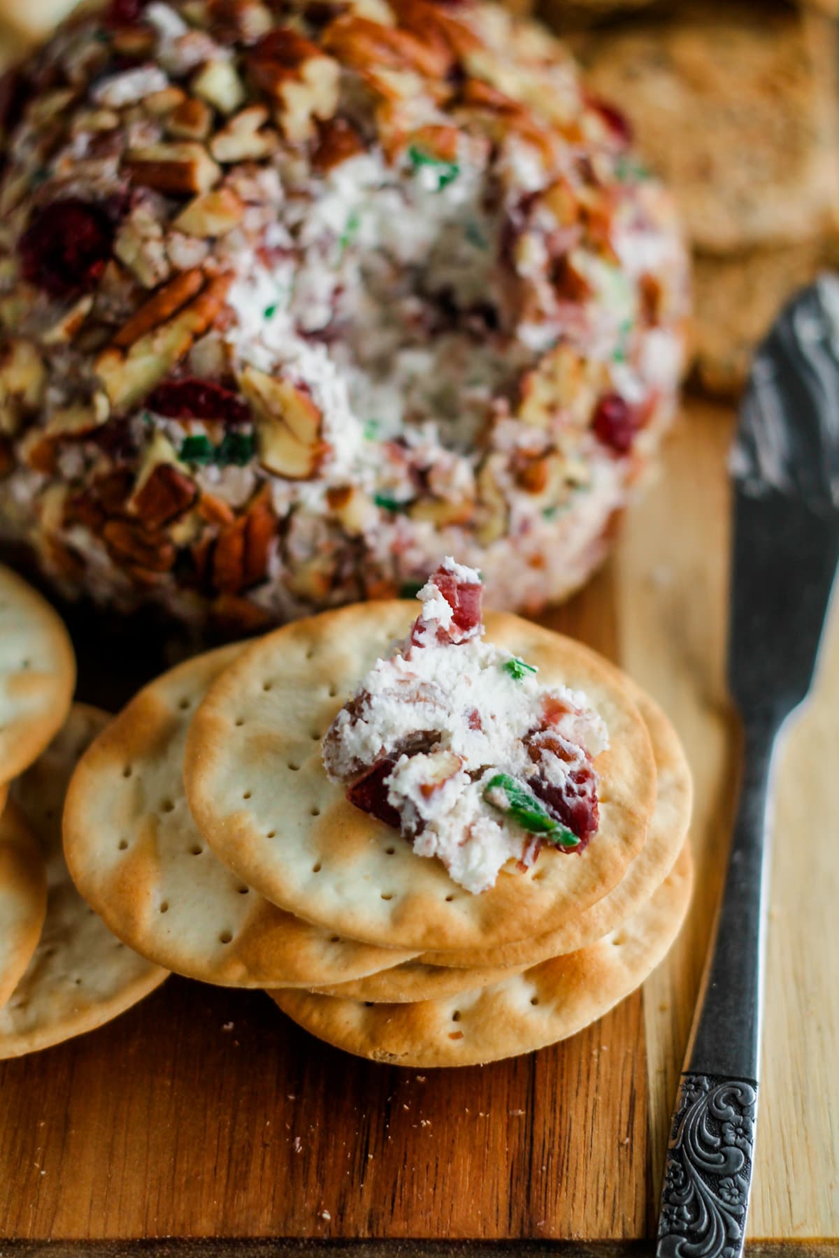 A wooden board with a cranberry pecan cheese ball and a stack of crackers.