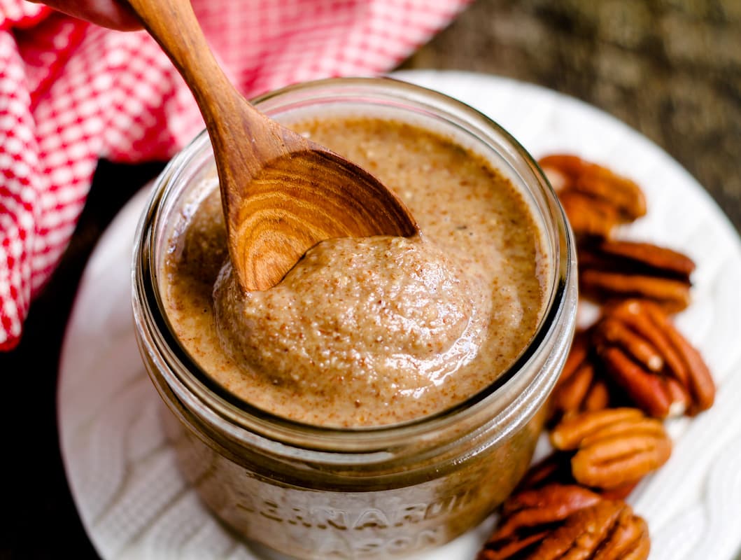 A spoon scooping pecan butter from a jar.