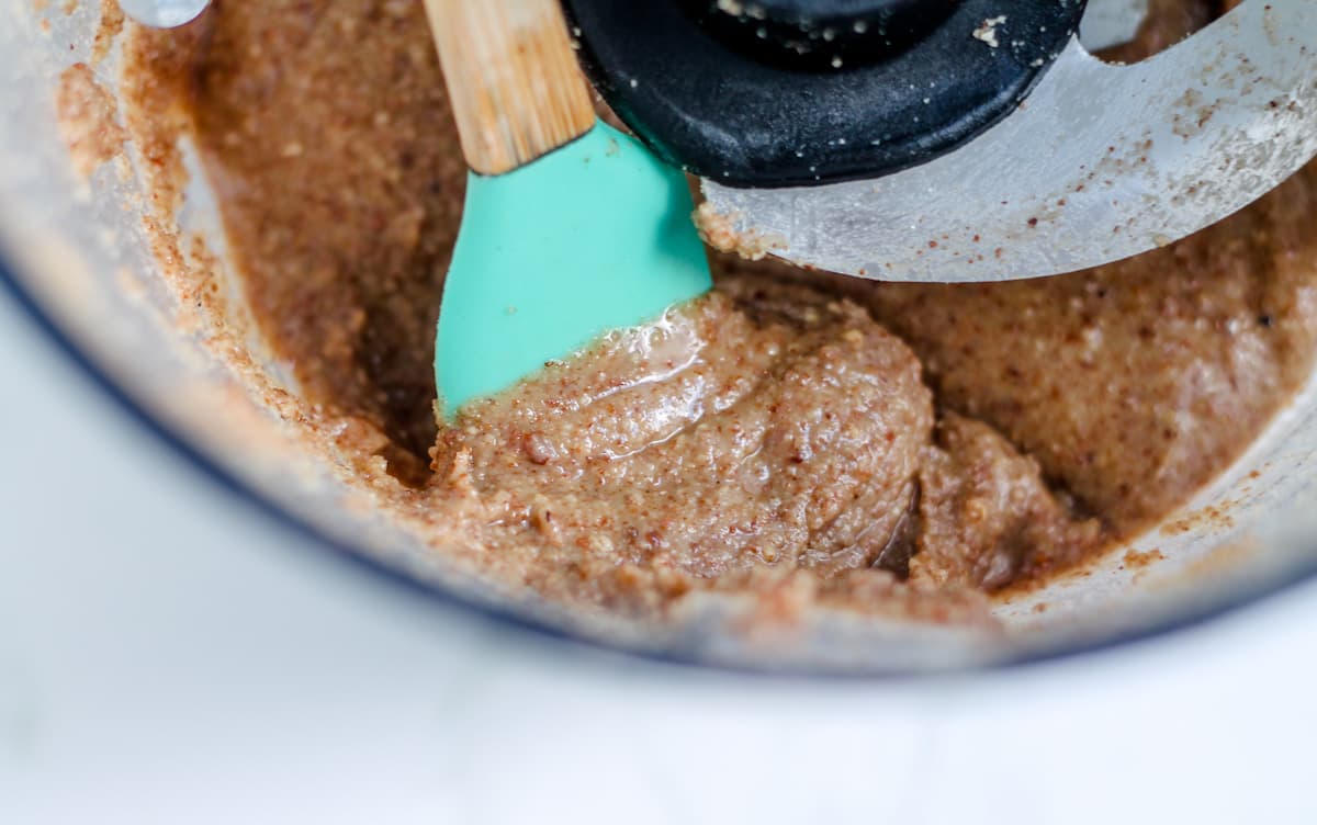 A spatula stirring nut mixture in a food processor.