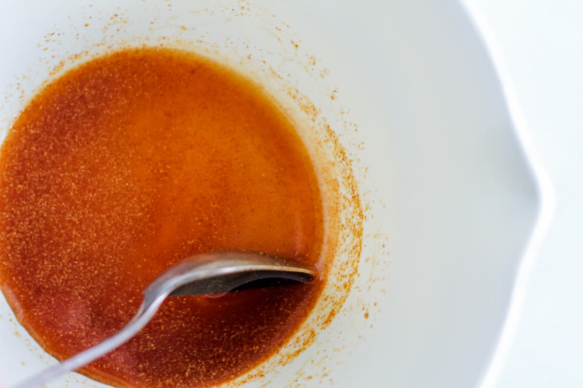 A spoon stirring maple syrup and cayenne powder in abowl.