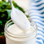 A spoon being dipped into a jar of homemade ranch dressing.