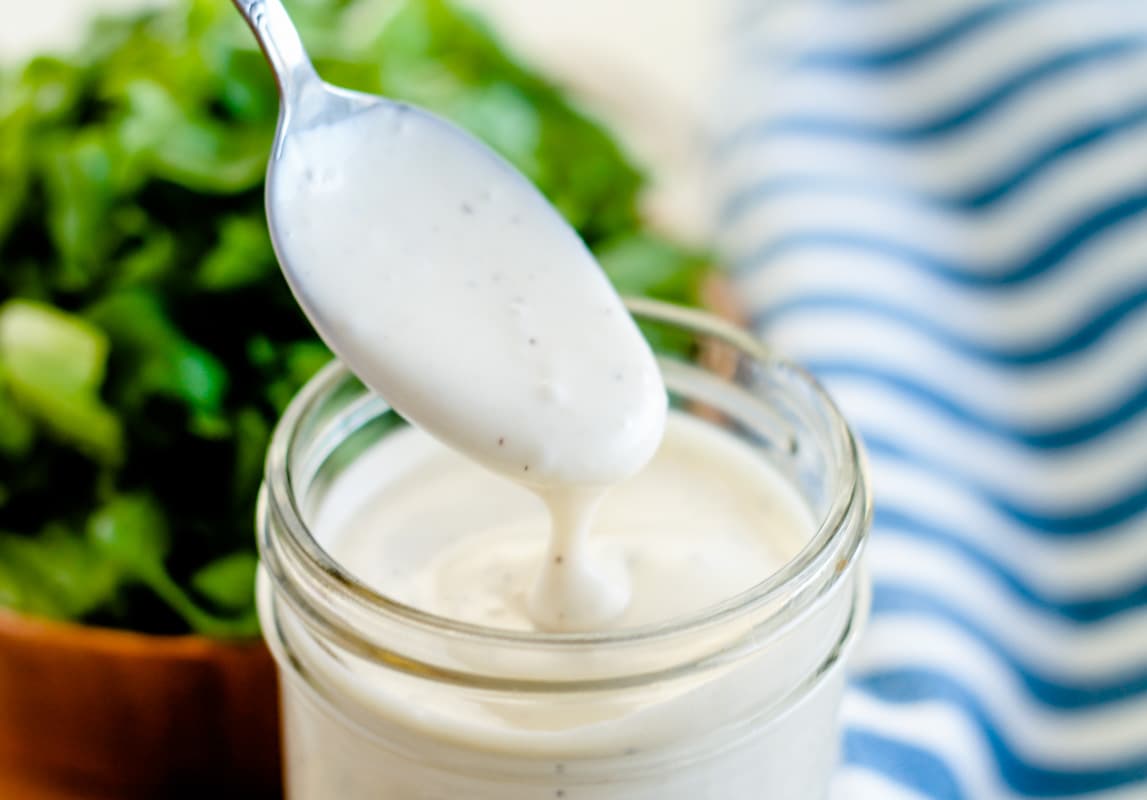 A spoon being dipped into a jar of homemade ranch dressing.