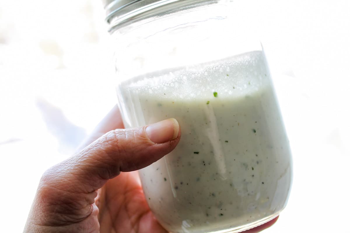 A hand holding homemade dressing in a jar.